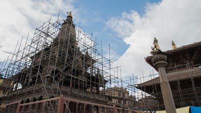 A temple in Kathmandu, Nepal, is being rebuilt with lots of scaffolding around it under a cloudy sky.
