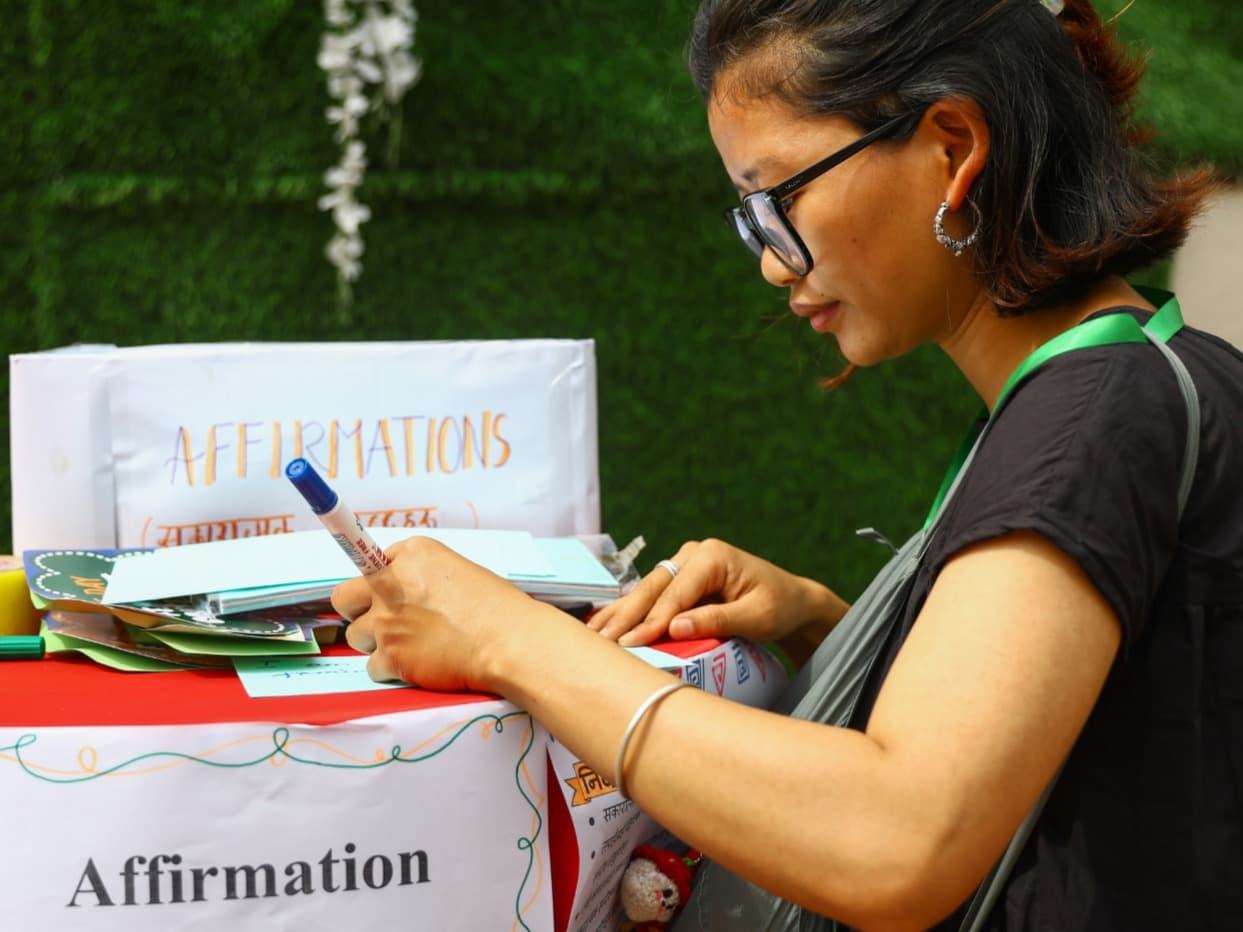 A woman with glasses writes on an "Affirmation Cards" display at the "One-day Feminist Conference 2025."