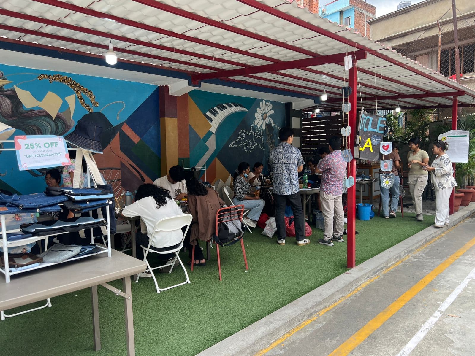 People participating in a creative upcycling event under a covered outdoor space, surrounded by colorful murals and handmade crafts.