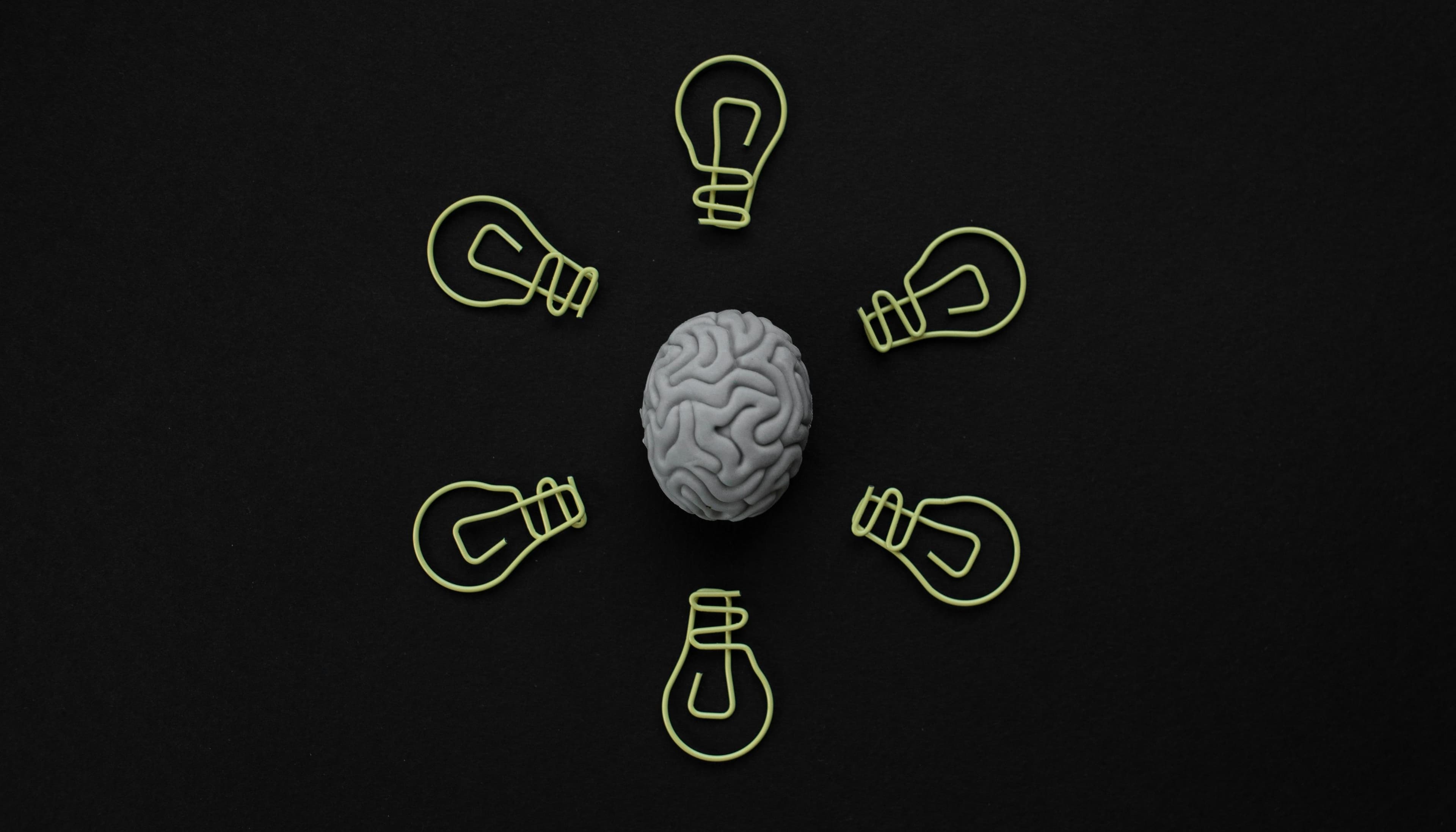 A grey brain model surrounded by seven yellow lightbulb outlines on a black background.