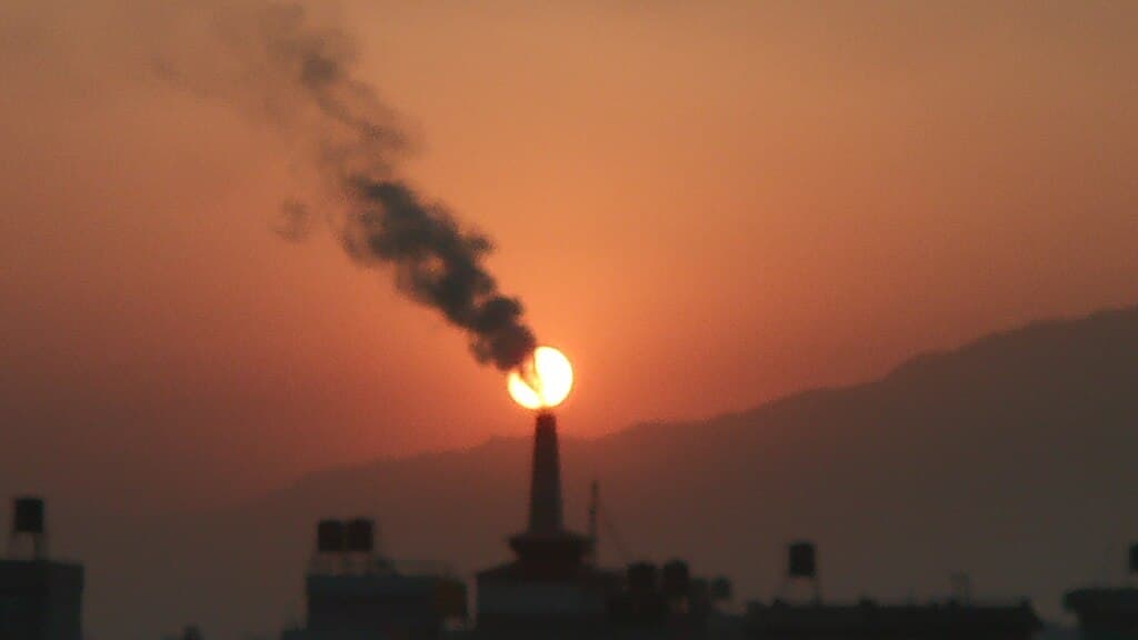 A brick kiln chimney in Kathmandu emitting smoke that merges with the sunset, symbolizing Nepal’s worsening air pollution and industrial emissions problem.